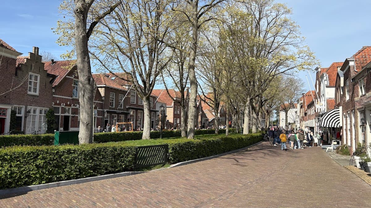 People walking on a brick street lined with historic brick buildings and tall trees in a European town.