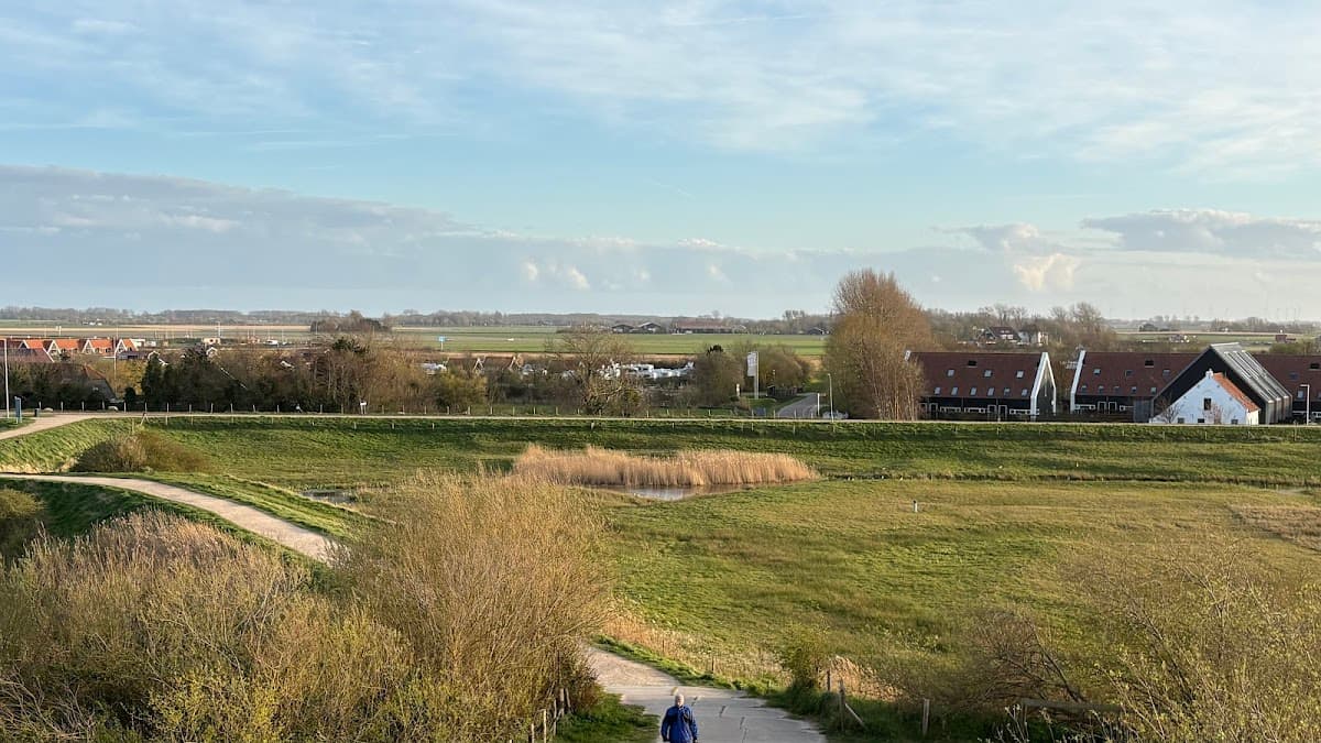Person walking on a path through a rural landscape with green fields, trees, and traditional houses.