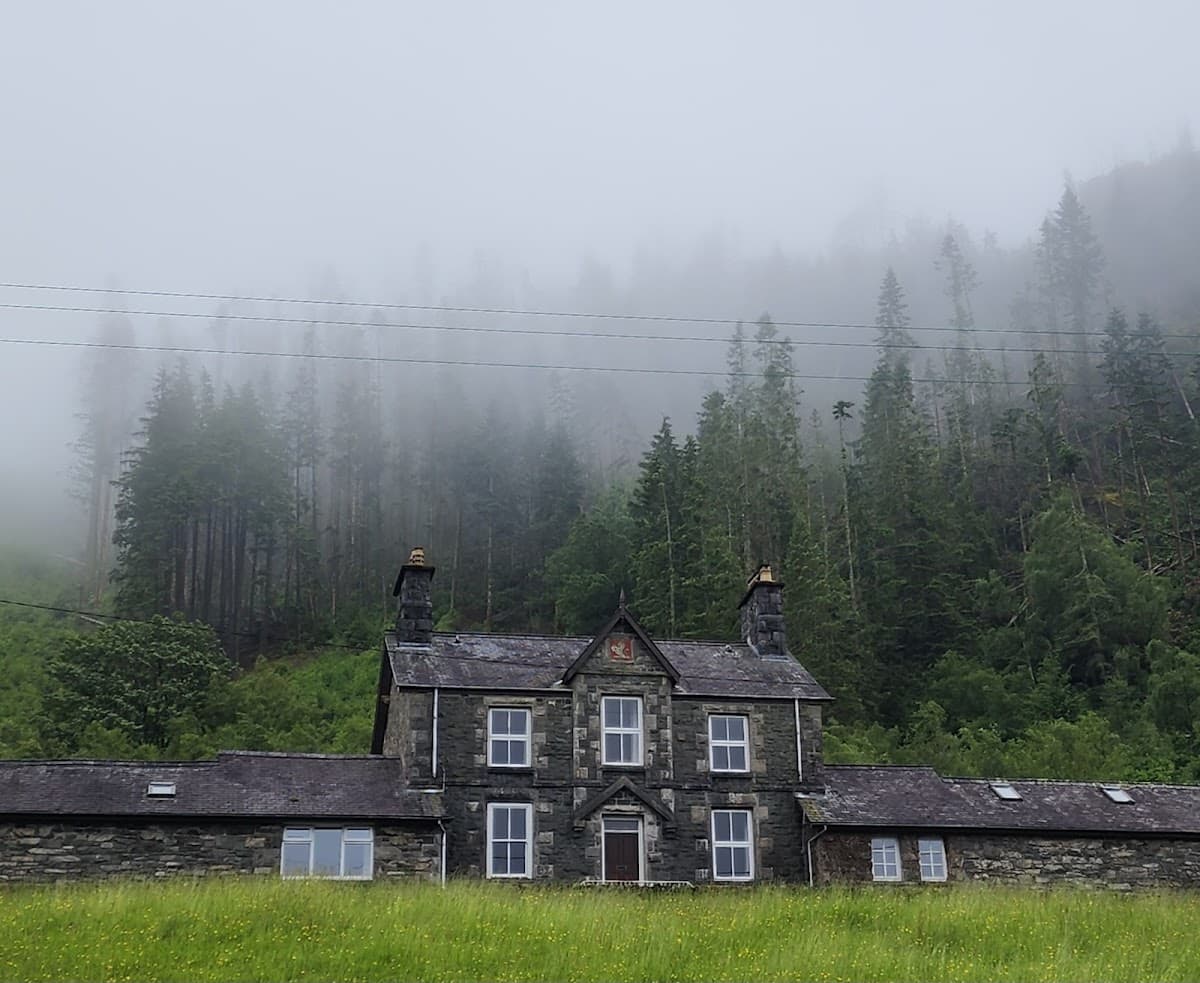 Stone house with slate roof set against foggy pine forest and mountain slope