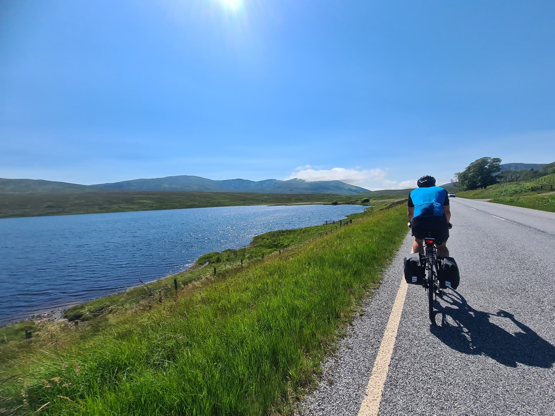 Cyclist riding along a lochside road with hills and bright blue sky