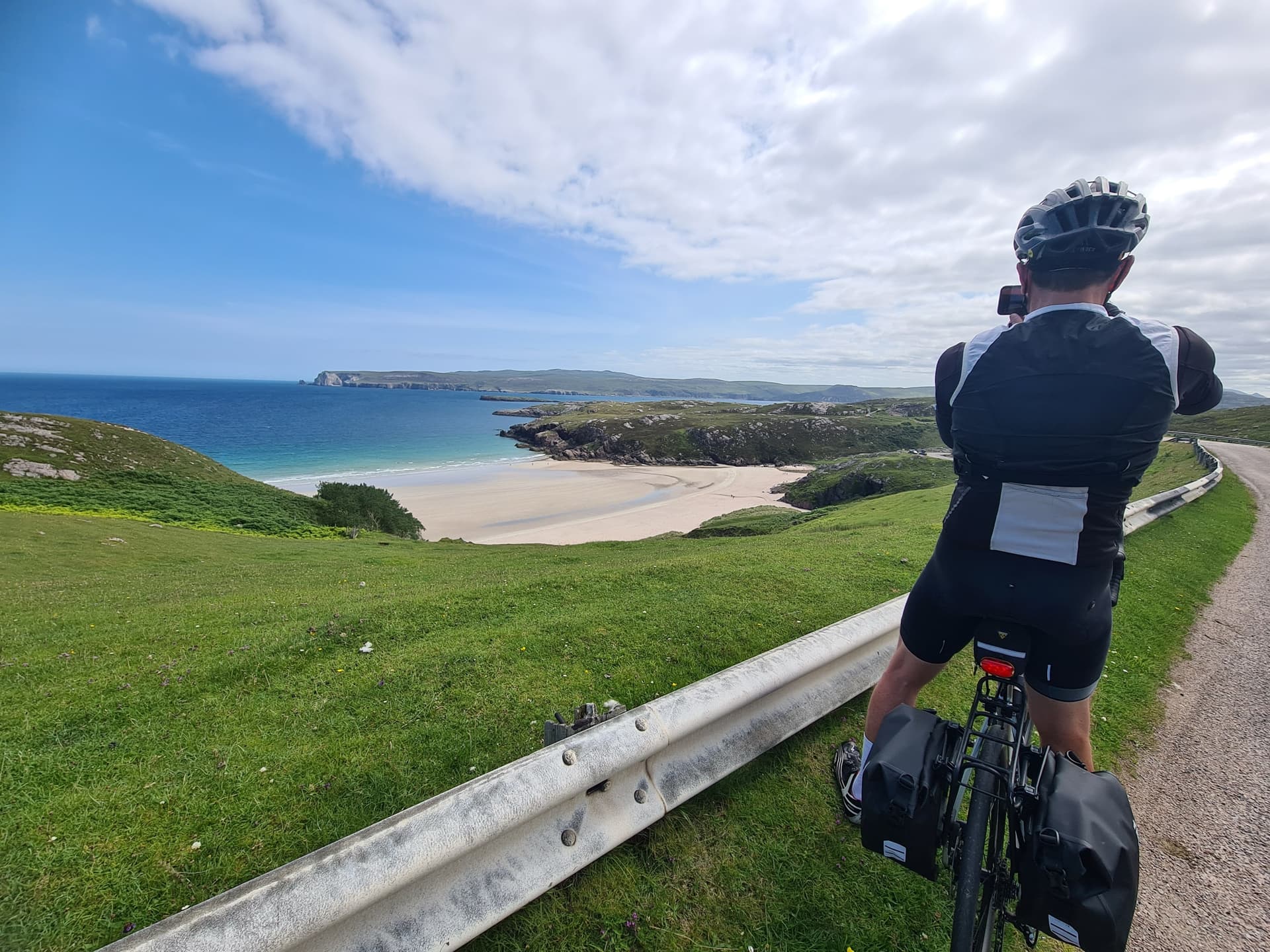 Cyclist photographing a sandy bay from a coastal road