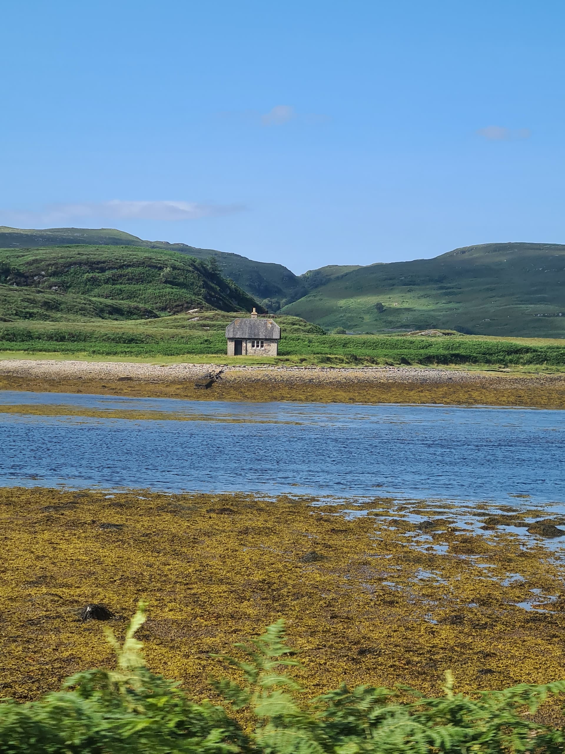 White cottage across a sea loch with green hills and blue sky